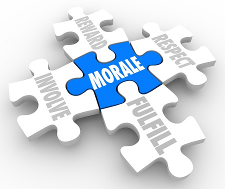 A 3D rendering of five interlocking puzzle pieces arranged on a plain, light grey surface. A bright blue puzzle piece sits in the very center with the word